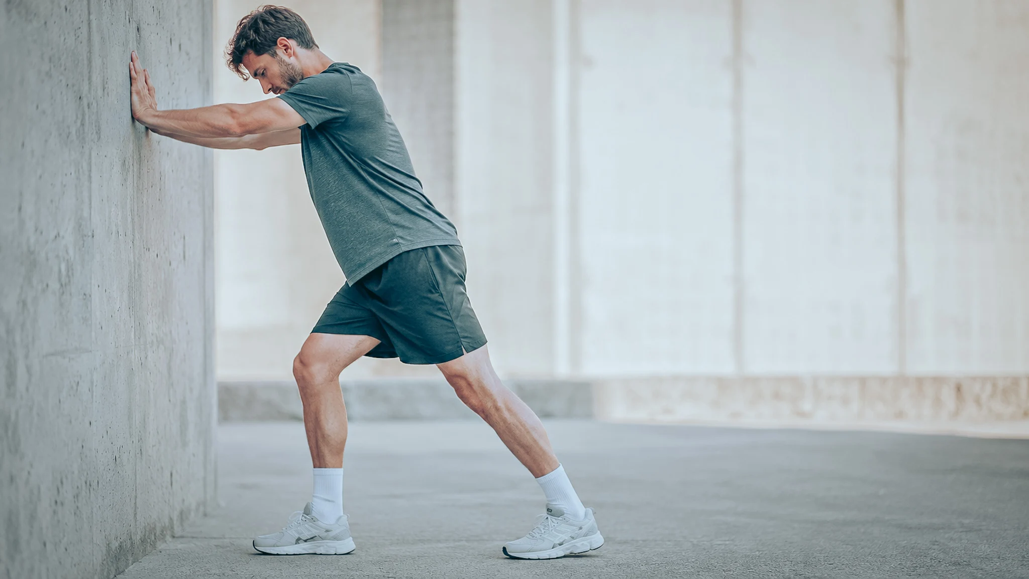 Homme s'étirant contre un mur, en tenue sportive, illustrant les bienfaits des compléments.