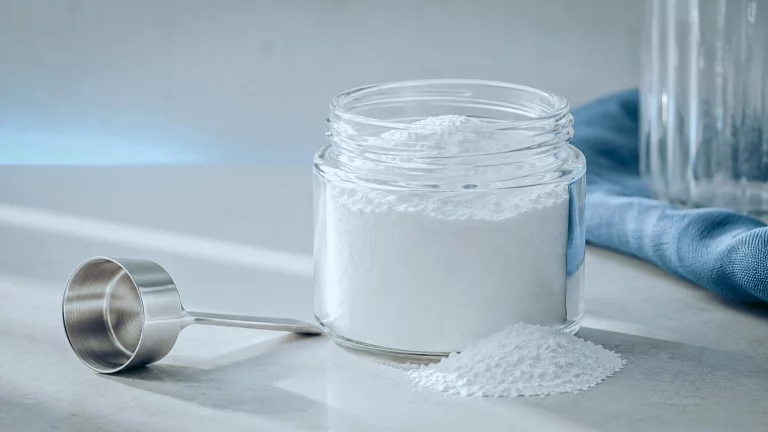 Pot en verre de créatine monohydrate en poudre avec sa dosette, posés sur un plan neutre