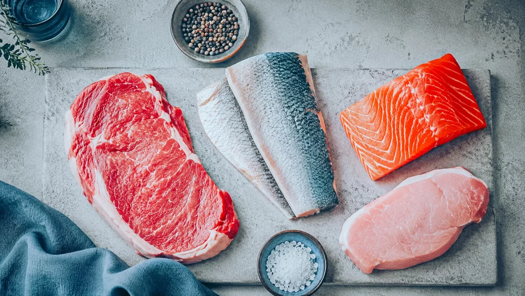 Sources alimentaires de créatine : bœuf, poissons et porc crus disposés sur une planche