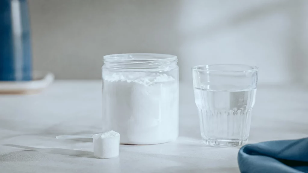 Pot de créatine en poudre, dosette et verre d'eau pour choisir une créatine simple et pure