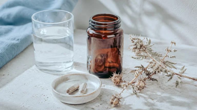 Pot de Tribulus, deux gélules sur une coupelle, verre d'eau et brin de plante séchée.