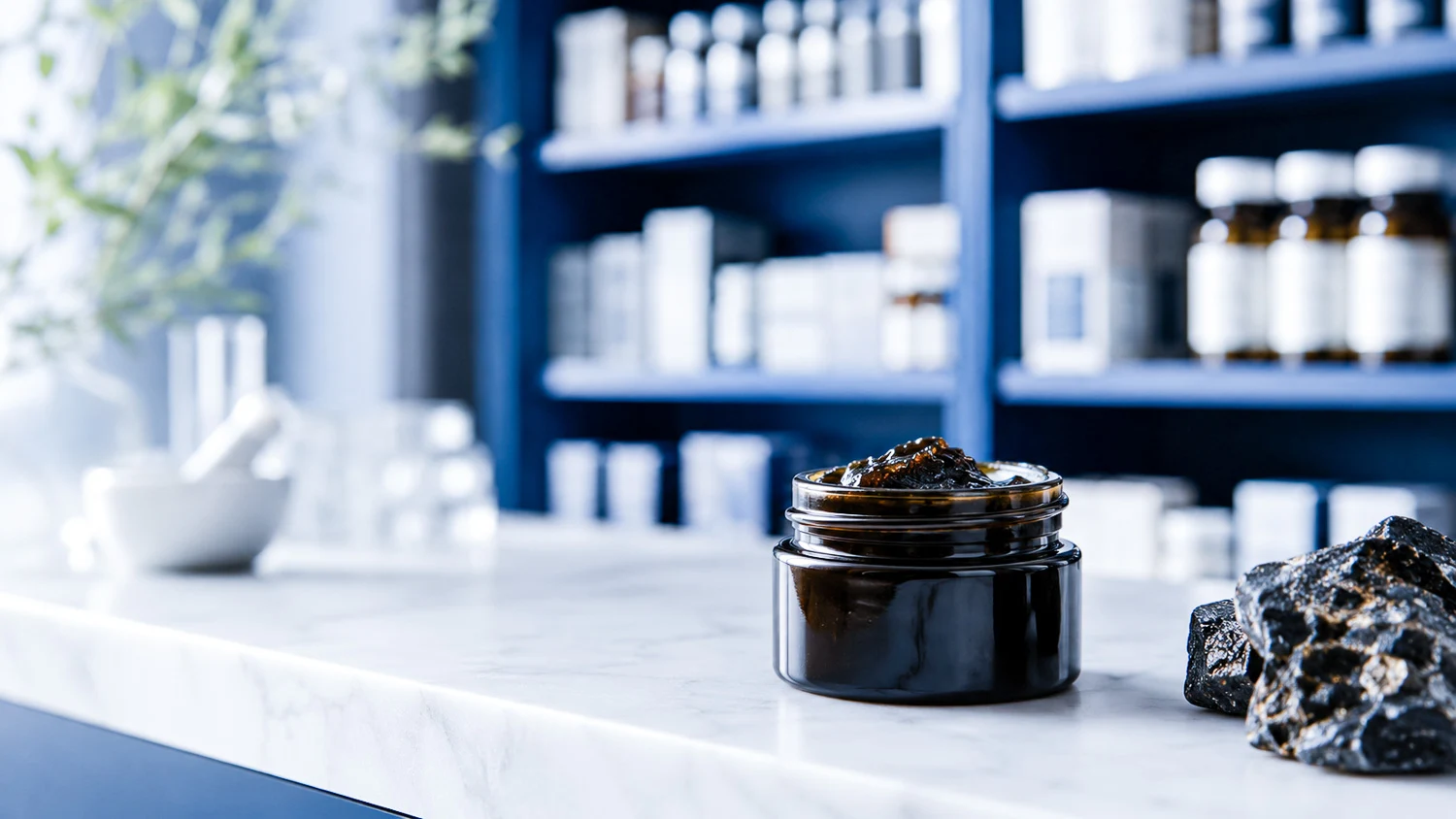 Résine de shilajit dans un pot sur un comptoir, avec des produits de santé en arrière-plan.